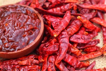 Terasi chili sauce in a wooden bowl and surrounded by dried chilies piled up around it. With a...