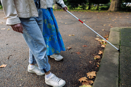 Blind woman using white cane walking in a park with friend