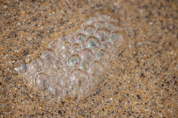 Iridescent bubbles floating on wet sandy beach
