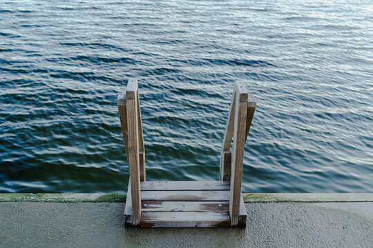 Minimalistic shot of a wooden ladder leading into the blue water