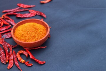 Chili powder in a wooden bowl and dried chilies or Capsicum annuum L, scattered around it. With a close look.
