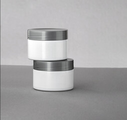 Moisturizing balm, facial mask jars. White containers with feminine skin care product. Mockups with balancing cream on gray background.