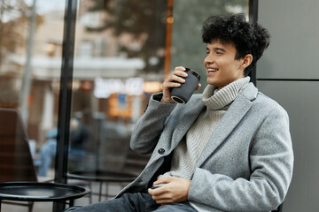 Fashionable young man smiling and holding a coffee cup in front of a window
