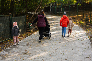 A family, including children and a stroller, walk along a leafy path in a park during autumn. The scene captures the essence of togetherness and the beauty of fall.