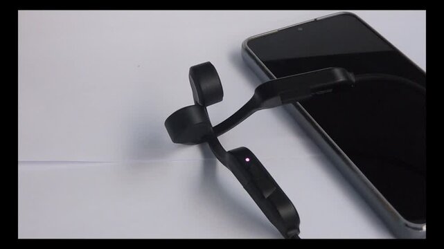 a bone conduction headphones connected to a cellphone is marked by a blue indicator light flashing
