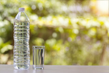 A clear plastic water bottle and a glass of water are placed on a table against a blurred background of green leaves.