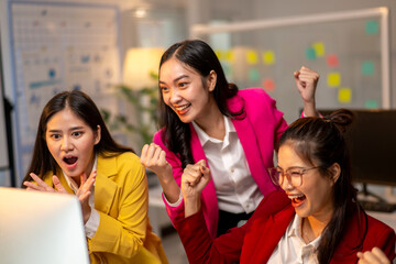 Three women are standing in front of a computer screen, all of them wearing pink
