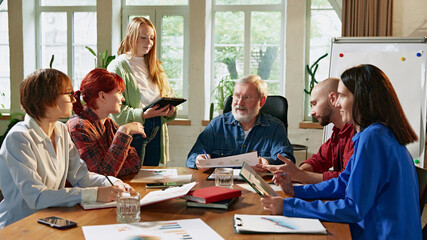 Team of diverse business professionals discussing strategies around conference table in modern,...