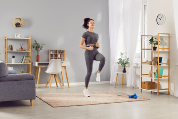 Woman runs in place as part of her home workout session. She focuses on fitness and cardio training, staying active and healthy through regular jogging, running and sport in home gym.