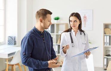 Young man standing in office, listening carefully to female doctor. Physician or cardiologist with...