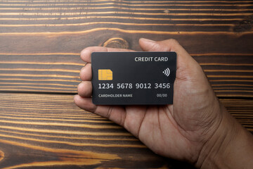 Human hand holding a debit or credit card with wooden background