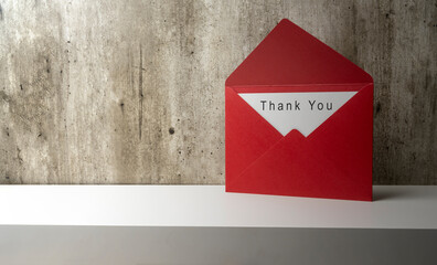 Red envelope and postcard with white card with words Thank You written on it on the shelf wall