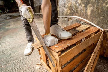 Workers in safety vest and gloves using hand saw to on wood at workshop