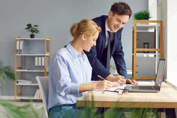 Enthusiastic and positive business colleagues working together with laptop and engaged in paperwork...