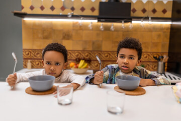 Two african american kids sitting at the table and having breakfast