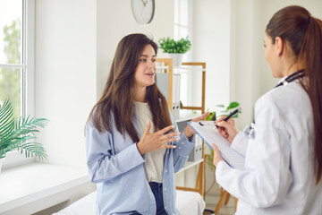 A young woman in a clinic talks to a doctor about her health, close-up. Woman doctor listens to patient and writes down symptoms. Concept medical consultation and diagnosis of disease