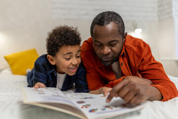 Naklejka premium Dark-skinned man looking at the pictures in the boom together with his son