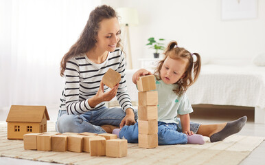 Mother and child engage in building a tower with wooden cubes together at home, enjoying family leisure time. Shared playtime fosters closeness, creating joyful moments in domestic environment.