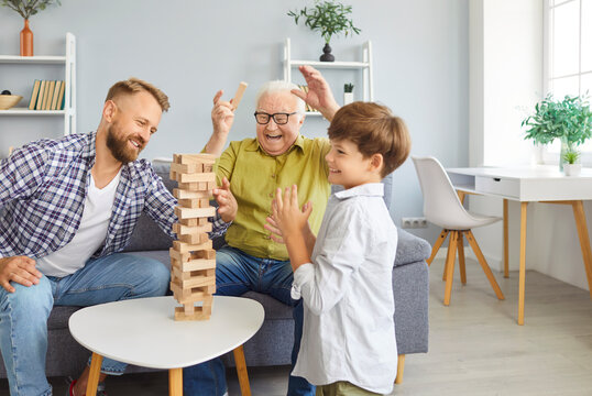 Overjoyed family of three generation men, senior grandfather, adult father, child grandson playing at home jenga board game together, making tower building, weekend celebrating father's day holiday
