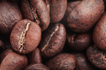 Сlose-up of roasted coffee beans, highlighting their rich, dark brown color and textured surface. The beans display natural cracks and grooves, indicating a medium to dark roast. Focus on coffee beans