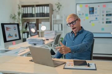 Obraz premium Surprised mature entrepreneur having video conference with colleagues on laptop, discussing project results and financial strategy, working in modern office