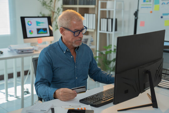 Senior business manager concentrating on entering credit card details on computer, making secure online transaction in modern office workspace - Powered by Adobe