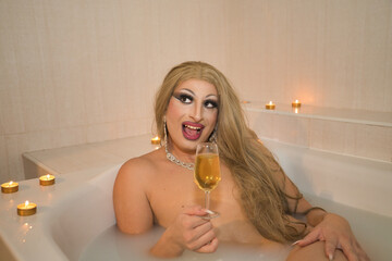 Drag queen, blonde, attractive, taking a milk bath in a jacuzzi, with a glass of wine in her hand...