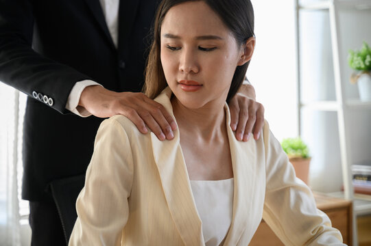 A male colleague or supervisor places a hand on the shoulder of an uncomfortable-looking female employee. Concept issues of sexual harassment, inappropriate behavior, and workplace dynamics.