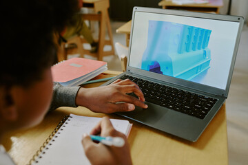 Person sitting in classroom while learning 3D modeling with laptop in front of them and notebook for jotting down notes. Focus on laptop screen showing 3D model