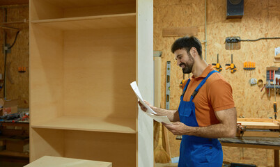 Carpenter looking at paper sheet with project blueprint at woodshop