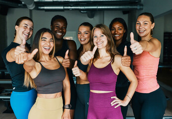 Fit group of diverse young women in sportswear smiling and giving the thumbs up after an exercise class together in a pilates gym
