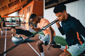 Trainer showing a fit young man how to workout with a barbell during a strength training workout session at the gym