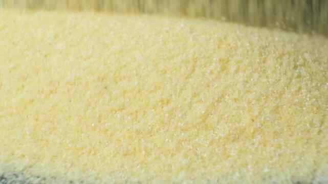 Uncooked semolina cereal pouring on black background slow motion