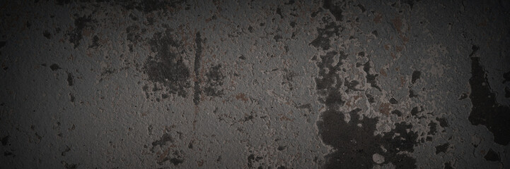 Texture of the old wall. Rough grungy surface of painted plastered concrete wall with spots, cracks, noise and grain. Dark wide panoramic background for design. Shaded vintage texture with vignette.