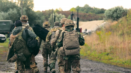 Soldiers walking in the field, armed and equipped. A group of soldiers in full combat gear walks...