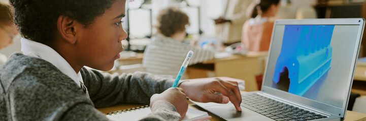 Student engaging in educational activities on laptop while holding pen, surrounded by classmates in...
