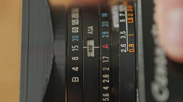 Static top shot of caucasian hands adjusting different settings on an old vintage film camera. Adjusting asa aputure and shutter speed.