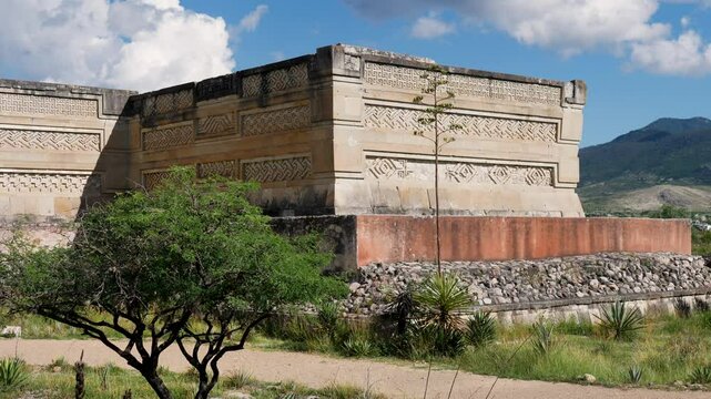 Slow motion landscape of tree and pathway in front of historic castle ruin walls of Mitla archaeological site in Zapotec valley Oaxaca city Mexico sacred culture tourism town