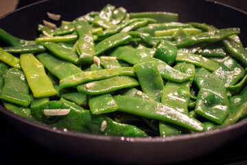 Sauteed flat beans with garlic and spices in a pan The vibrant green beans are being cooked in oil for a traditional Italian side dish to accompany meat dishes
