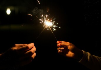 Two hands holding burning sparklers, celebrating new year's eve or other special occasion