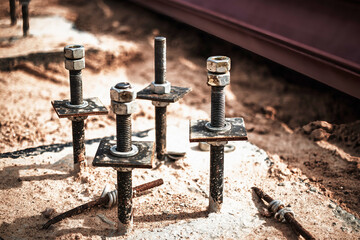 Reinforced concrete foundations with embedded bolts and nuts during construction at an outdoor site...