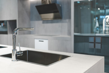 a sleek and modern kitchen sink and faucet set against a backdrop of dark cabinetry and a marble countertop. The faucet is a single-handle design with a tall, arched spout and a black matte finish.