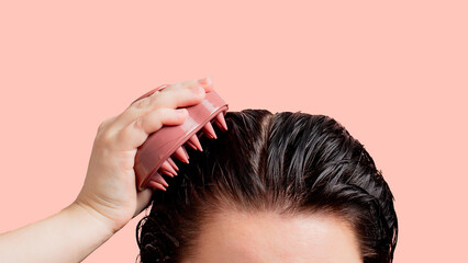 Woman doing scalp massage with pink massager. Part of the female head with vet clean hair on the pink background. Isoalted image. Mock up for design and banners