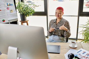 A cheerful bald woman engages with her work, sipping coffee and smiling at her screen.