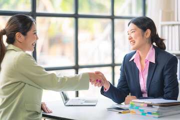 Two Asian businesswomen are deeply engaged in a discussion about data analysis work on a computer screen with graphs and charts. Showcase teamwork