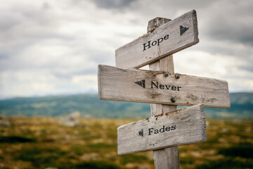 hope never fades text quote written on wooden signpost at the crossroads outdoors in nature.