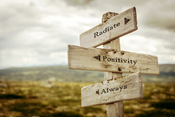 radiate positivity always text quote written on wooden signpost at the crossroads outdoors in nature.