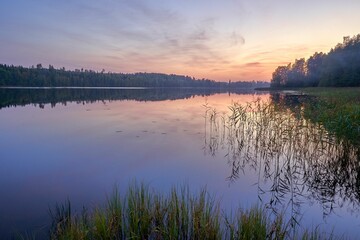 Sunset over a tranquil lake with forest reflections.