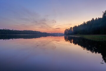 Obraz premium Sunset over a tranquil lake with forest reflections.