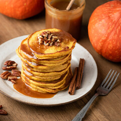 Breakfast pumpkin pancakes with caramel and pecan nuts on a wooden background